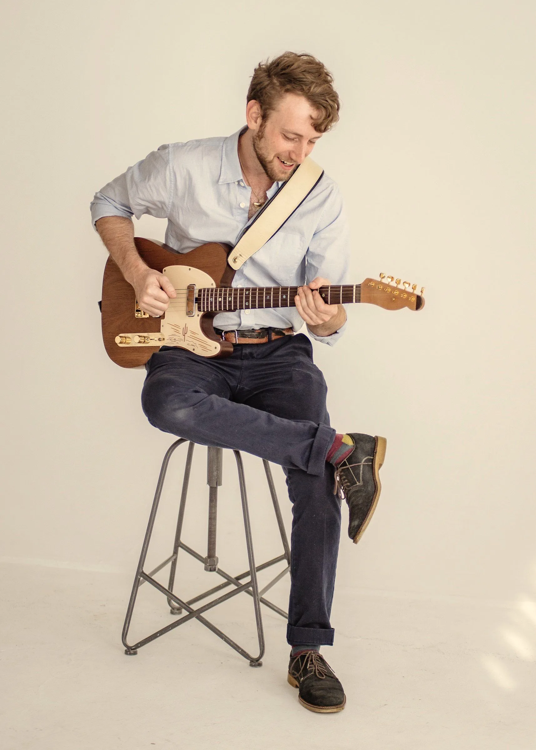Jordan Lovinger, The Grand Guitarist, playing a Telecaster on a stool in a white studio